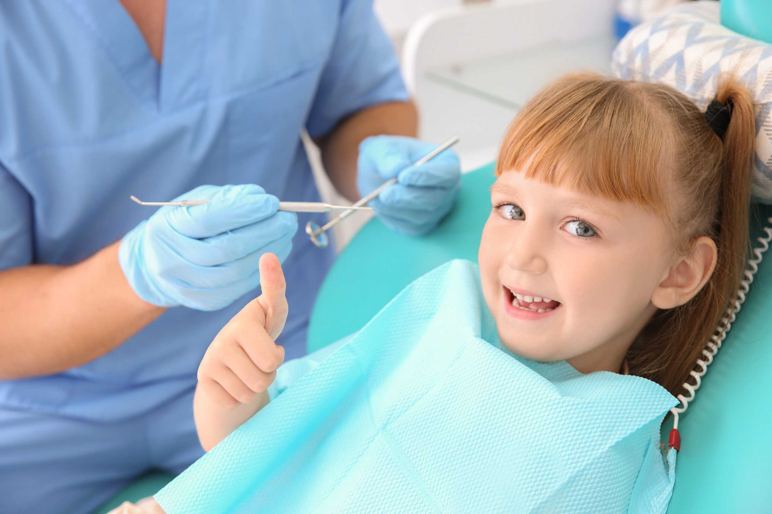 Cute little girl showing thumb-up gesture at dentist's office